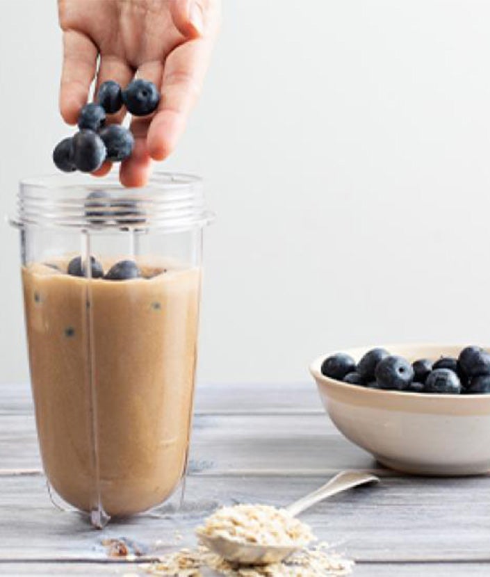 hands adding whole blueberry into blender