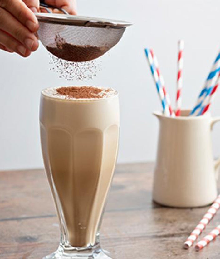 sieving chocolate powder onto cappuccino milkshake