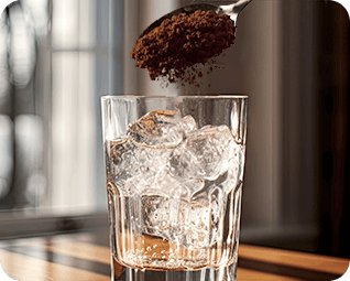 Instant coffee being put into glass of ice water.