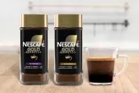 NESCAFÉ® Gold Espresso Intense and Blonde packaging next to a mug filled with espresso on a wood surface.