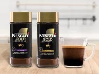 NESCAFÉ® Gold Espresso Intense and Blonde packaging next to a mug filled with espresso on a wood surface.